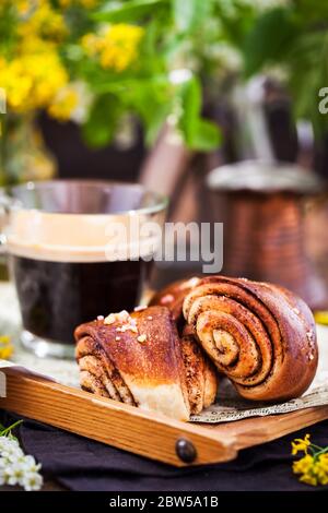 Dolci fatti in casa alla cannella e cardamomo (panini) e una tazza di caffè nero Foto Stock