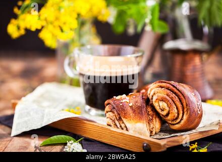 Dolci fatti in casa alla cannella e cardamomo (panini) e una tazza di caffè nero Foto Stock
