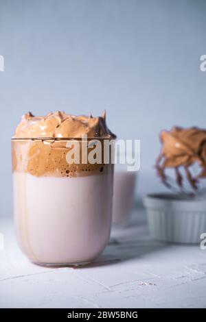 Caffè Dalgona con latte in un bicchiere su fondo testurizzato bianco. Caffè coreano. Vista ravvicinata. Foto Stock