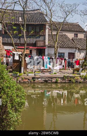 Tongli, Jiangsu, Cina - 3 maggio 2010: Linea di lavanderia colorata riflessa in acqua verde del canale sotto il cielo azzurro chiaro. Case dai tetti scuri, un uomo e s. Foto Stock