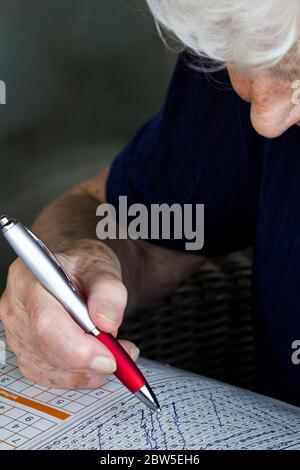 Donna anziana che fa crossword puzzle per mantenere mentalmente attivo. Foto Stock