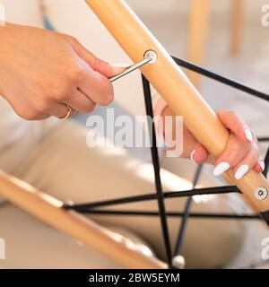 Donna auto montaggio una poltrona, serraggio bulloni sciolti con una chiave esagonale per mobili, primo piano Foto Stock