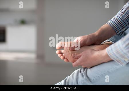 Mani dell'uomo che ti danno il massaggio del piede per alleviare il dolore dopo una lunga passeggiata, a causa di scarpe scomode, che soffrono di piedi piani, da vicino, focu morbido Foto Stock