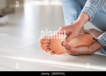 Mani dell'uomo che ti danno il massaggio del piede per alleviare il dolore dopo una lunga passeggiata, a causa di scarpe scomode, che soffrono di piedi piani, da vicino, focu morbido Foto Stock