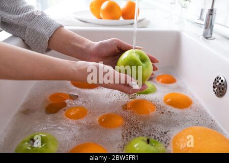 Mani di donna che lavano la mela sotto il rubinetto nella cucina del lavandino, ammollando la frutta in acqua saponata lavano accuratamente dopo il deposito. Foto Stock