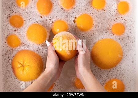 Vista dall'alto delle mani di donna che lavano l'arancia matura, pompelmo sotto il rubinetto nella cucina del lavandino, ammollando la frutta in acqua saponata lavano accuratamente dopo il Foto Stock
