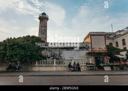 I giovani si siedono sul marciapiede di fronte ad un vecchio faro nella città di Pondicherry, sulla costa orientale dell'India Foto Stock