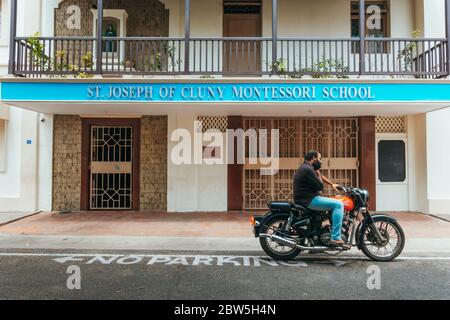 Un uomo parla su un telefono cellulare mentre si siede su una moto di fronte a San Giuseppe di Cluny Montessori Scuola, Città Bianca, Pondicherry, India Foto Stock