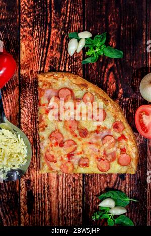 Vista dall'alto di salsiccia, prosciutto, pepe e pizza al formaggio su sfondo scuro in legno con pezzi di ingredienti freschi Foto Stock