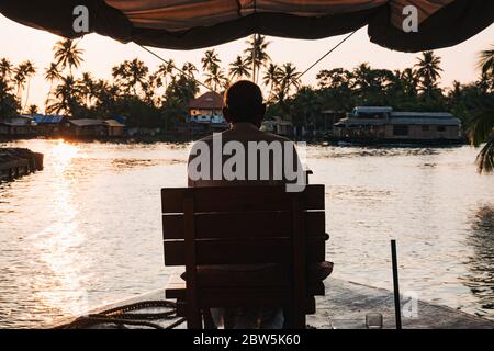 L'autista di una casa galleggiante Keralan guida la barca da un sedile sulla prua, come il sole tramonta Foto Stock