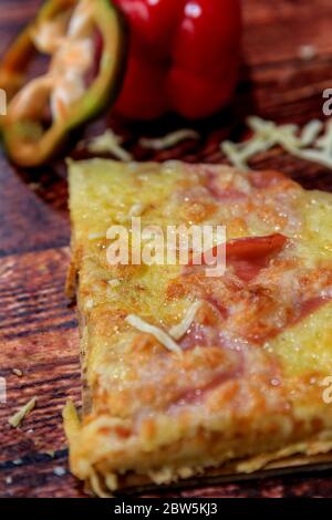 A metà fetta di pizza con prosciutto, salame e formaggio su fondo di legno con ingredienti freschi sulla parte superiore Foto Stock