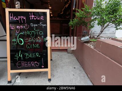 un cartello con la lavagna davanti a un pub offre happy hour con una lista di bevande durante il coronavirus o la pandemia del covid-19 Foto Stock