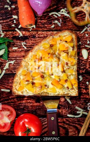 Vista dall'alto della pizza a sapori contrastanti con salsiccia calda, ananas dolci e mango circondati da verdure fresche su un tavolo di legno scuro Foto Stock