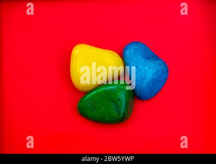 Multicolore Pebbles naturali pietra verde, blu e gialla isolata su sfondo rosso con spazio per copiare testo e parole. Pietra colorata naturale di pebble Foto Stock