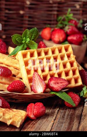 Waffle con fragole fresche e foglie di menta su un vecchio tavolo di legno. Foto Stock