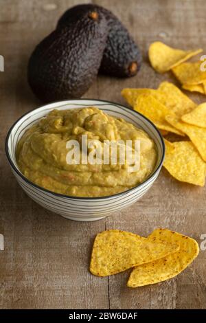 Guacamole fresche fatte in casa con patatine di tortilla e avocado sullo sfondo di un tavolo di legno Foto Stock