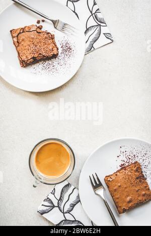 Vista dall'alto di una tazza di caffè e due piatti da dessert con torta di brownie su sfondo rustico bianco. Foto Stock