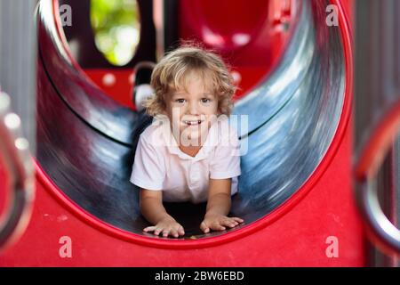 Bambino che gioca sul parco giochi all'aperto. Bambini a giocare sulla scuola o asilo nido cantiere. Capretto attivo sulla colorata scivolo e altalena. Una sana attività estiva per chi Foto Stock