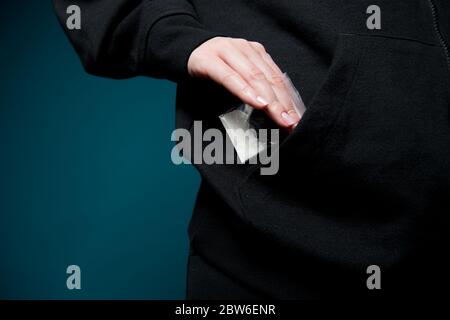 una mano femminile toglie un sacchetto di eroina o cocaina da una tasca, primo piano. Foto Stock