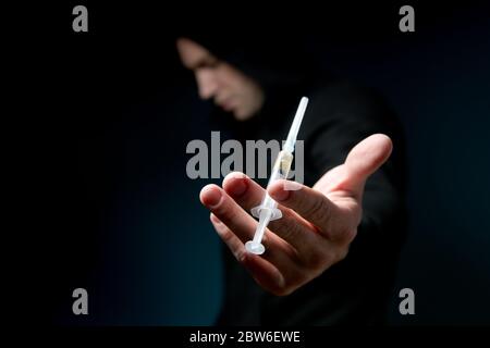 la silhouette scura di un uomo tiene fuori un telaio con una dose di farmaco in una siringa, fuoco selettivo Foto Stock