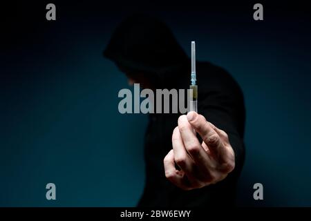 Un uomo tiene fuori una siringa con un farmaco e nasconde il suo viso. Sagoma scura con siringa Foto Stock