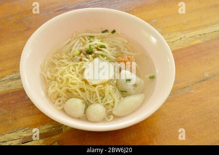 Tagliatelle cinesi all'uovo che condgono gnocchi di pesce e pallina di gamberi in zuppa trasparente sulla ciotola Foto Stock