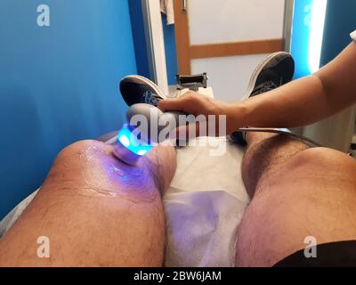 Il fisioterapista sta applicando la terapia a ultrasuoni sulle lesioni al ginocchio con il trasduttore della testa a ultrasuoni, movimento blured Foto Stock