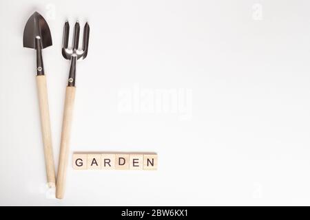 Attrezzi per giardinaggio a casa. CopySpace per testo, vista dall'alto. Flatlay su sfondo bianco. Testo GIARDINO fatto di cubo di legno. Lettering GIARDINO, lettering i Foto Stock