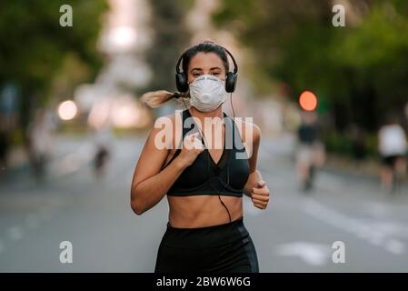 Donna runner con maschera medica. Correre nel parco. Coronavirus pandemico Covid-19. Maschera facciale sterilizzante chirurgica per uso sportivo e attivo in quarantena Foto Stock