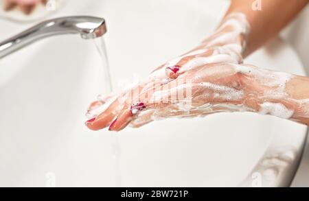 Giovane donna che le lava le mani sotto rubinetto d'acqua con sapone. Dettagli sulla pelle ricoperta di suds. Concetto di igiene personale - coronavirus covid-19 focolaio Foto Stock