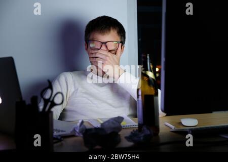 Un giovane esausto in bicchieri che sperimenta la tensione durante una tarda notte al lavoro, bevve una birra per rilassarsi, si addormenta dalla fatica. Lavori di lavoro, pigrizia, Foto Stock