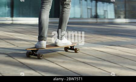 Skateboarder maschile a cavallo e praticare il longboard in città, all'aperto, in movimento, immagine ritagliata. Uomo in fondo alla strada con skateboard. Tempo libero, healt Foto Stock