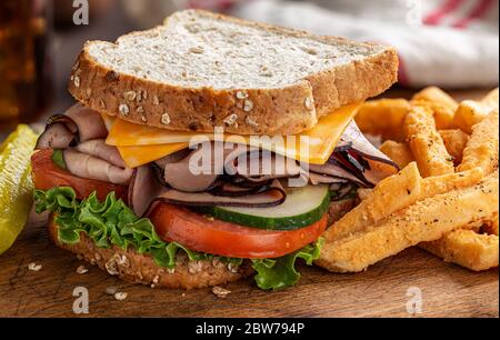 Primo piano di un sandwich di prosciutto e formaggio con lattuga, pomodoro e cetriolo su pane integrale su un tavolo di legno Foto Stock