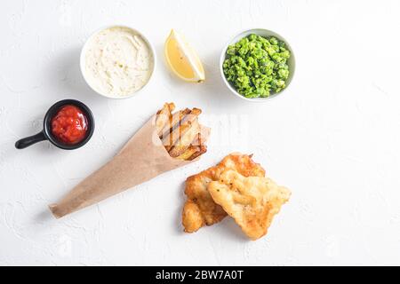 Componenti del tradizionale set britannico di pesce e patatine fritte di merluzzo, patatine fritte, fette di limone, salsa tartaro e piselli, ketCup di pomodoro Foto Stock