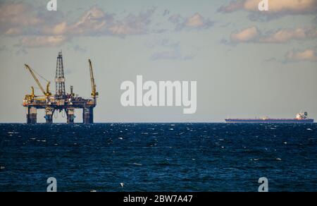 Piattaforma di perforazione di petrolio e gas in mare con nuvole blu e giorno di sole con nave da carico container Foto Stock