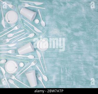 Oggetti in plastica monouso bianchi, come bottiglie, tazze, forcelle e cucchiai su sfondo blu Foto Stock