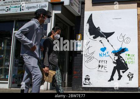 Wood Green, Londra, UK 30 maggio 2020 - i membri del pubblico che indossano rivestimenti del viso camminano oltre un murale con il messaggio 'NHS, TEST PPE, TOXIC TORIES OUT' nel nord di Londra. Credit: Dinendra Haria/Alamy Live News Foto Stock