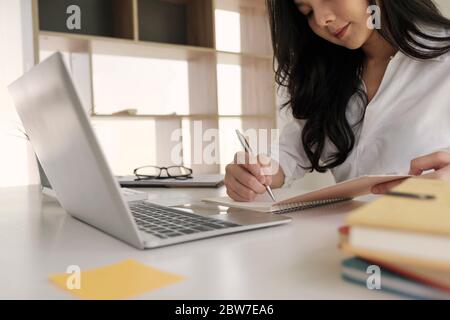Giovane donna di affari che prende note in notebook.on tavolo è un portatile per l'apprendimento online o business finance concetto Foto Stock