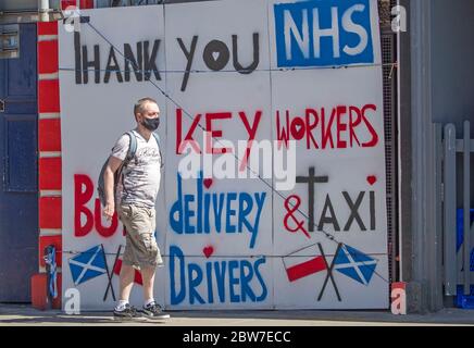 Una donna passa accanto a un poster che ringrazia l'NHS e i keyworker di Edimburgo, in quanto le persone possono incontrare familiari e amici all'aperto e giocare a sport come il golf e il tennis, mentre la Scozia sta entrando nella fase uno del piano del governo scozzese di sollevare gradualmente il blocco. Foto Stock