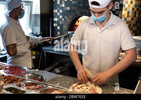 Chef preparano la pizza in pizzeria indossando maschere e protezioni durante l'emergenza di covid o coronavirus, riaprendo pizzerie e ristoranti Foto Stock