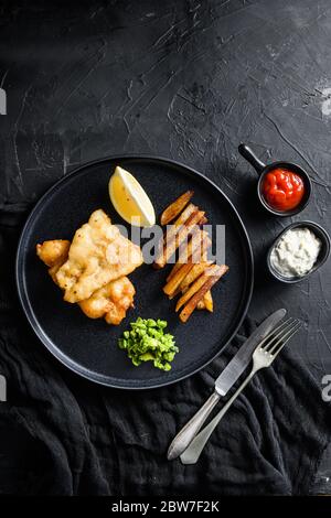 Pesce e patatine. Tradizionale piatto britannico di pesce fritto, patatine, piselli minati e salsa tartare e vista ketchup dall'alto, bac in pietra nera Foto Stock