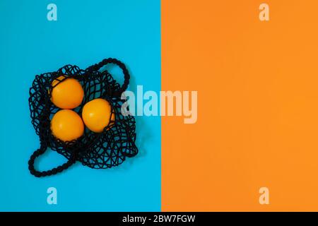 Concetto di zero sprechi. Borsa da shopping in mesh nera con arance su sfondo geometrico di colore blu e arancione. Vista dall'alto, spazio di copia Foto Stock