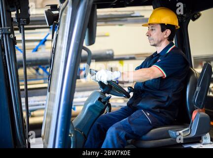 Un bel lavoratore di costruzione che guida un carrello elevatore in un impianto industriale Foto Stock