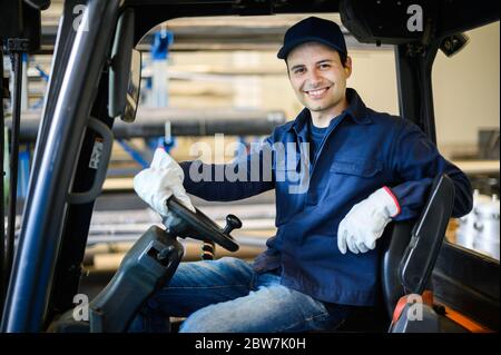 Un bel lavoratore di costruzione che guida un carrello elevatore in un impianto industriale Foto Stock