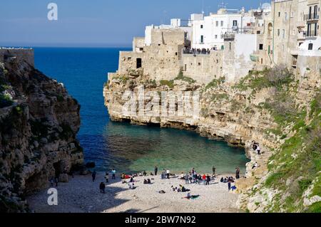 POLIGNANO A MARE, ITALIA - 29 MARZO 2018: Persone sulla bella spiaggia lama Monachile con spettacolare vista di scogliere con grotte che si innalzano dal mare Adriatico in Foto Stock