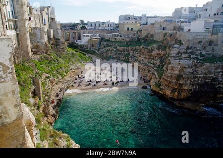 POLIGNANO A MARE, ITALIA - 29 MARZO 2018: Persone sulla bella spiaggia lama Monachile con spettacolare vista di scogliere con grotte che si innalzano dal mare Adriatico in Foto Stock