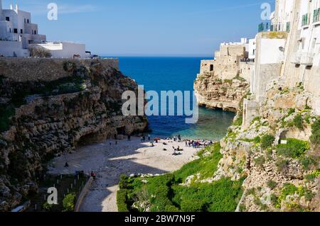 POLIGNANO A MARE, ITALIA - 29 MARZO 2018: Persone sulla bella spiaggia lama Monachile con spettacolare vista di scogliere con grotte che si innalzano dal mare Adriatico in Foto Stock