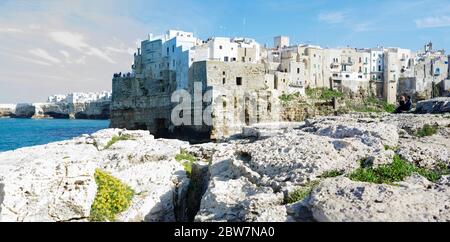 POLIGNANO A MARE, ITALIA - 29 MARZO 2018: Persone in riva al mare Adriatico con spettacolare vista di scogliere con grotte che si innalzano dal mare Adriatico a Pol Foto Stock