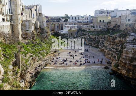 POLIGNANO A MARE, ITALIA - 29 MARZO 2018: Persone sulla bella spiaggia lama Monachile con spettacolare vista di scogliere con grotte che si innalzano dal mare Adriatico in Foto Stock