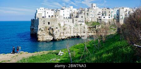 POLIGNANO A MARE, ITALIA - 29 MARZO 2018: Persone in riva al mare Adriatico con spettacolare vista di scogliere con grotte che si innalzano dal mare Adriatico a Pol Foto Stock